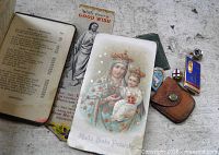 Open prayer book, holy card, bookmark, three pins and leather pouch displayed