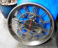 Front view of steel wall clock showing Roman numerals and gear design
