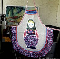 Full front view of linen apron with Matryoshka doll applique and floral ruffle