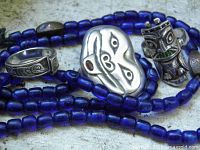 Close-up of blue glass beads with sterling rings and mask brooch