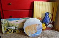 Overall lot showing three unframed paintings leaning against dresser