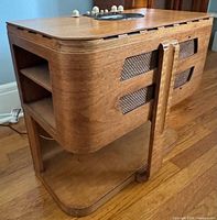 Left-front perspective showing blond wood cabinet, side shelf and grille