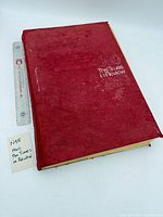 Front cover of red hardcover book with title visible and size reference