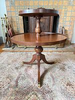 Full view of two-tier round wooden accent table showing turned column and tripod base with brass-capped feet