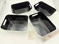 Four rectangular white and black plastic bins shown top view with ruler for scale
