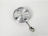 Front view of stainless steel wall clock with spoon pendulum attached