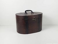 Front angled view of oval wood hat box trunk showing handle, latch and overall condition