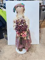 Full view of cloth doll on stand holding bouquet