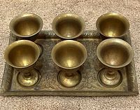 Top view showing six brass goblets seated in recessed wells on engraved tray