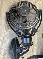 Overall view of black wall-mounted fan with bracket and grill