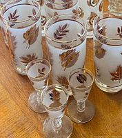 Group of frosted glasses showing both tumbler and cordial sizes with gold leaf design