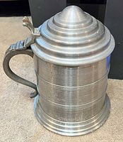 Side view of pewter-tone stein showing body, footed base, conical lid and handle