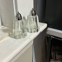 Front view of both glass shakers showing overall form and lids