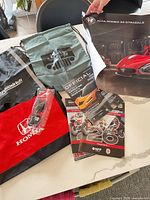 Group shot of all items: three bags, poster, brochures, sunglasses