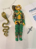 Serpentor figure with snake staff and dagger laid on countertop