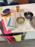 Lot overview showing plates, bowls, tea towels, placemat and wooden cup on countertop