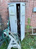 Full view of cabinet open with garden tools and hose reel visible