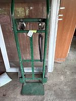 Front view of green steel hand truck showing frame, cargo strap, stair-climber wheels, fixed toe plate