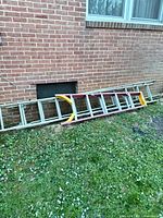 Three ladders leaning against brick wall; materials and colors visible