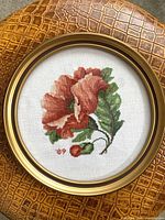 Front view showing full floral cross-stitch in round gold frame