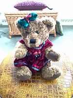 Front view of brown plush teddy bear in red velvet dress with green bow