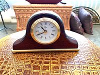 Front view of dark wood arch-top desk clock showing dial and gold bezel