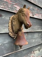 Side view of cast iron horse head with bell on weathered wall