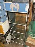 Front view of metal display shelf showing glass shelves and blue top panel