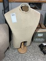 Front view of beige fabric torso mannequin on wood base; neck opening and fabric wear visible