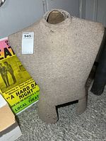 Front view of gray-brown fabric torso dress form showing neck, arm and leg openings, surface wear