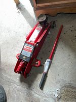 Full view of red hydraulic trolley jack and handle