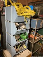 Side view of four blue stacked bins with yellow rope and assorted hardware visible inside