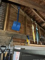 Blue plastic snow shovel, three umbrellas, hedge shears, garden wire coil visible on wall