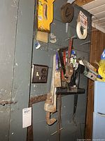 Group of hand tools hanging on door including pipe wrenches, paint brush, veneer edging and masking tape