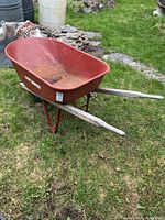 Side view of red True Temper wheelbarrow showing wooden handles, front tire, frame
