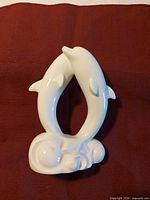 Front view of glossy white porcelain dolphin figurine on maroon background