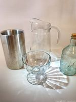 Front view of all four items: stainless container, glass pitcher, footed compote, aqua bottle