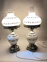 Pair of lit milk glass and brass hurricane table lamps with cords visible
