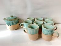 Side view of teapot with lid and seven matching mugs