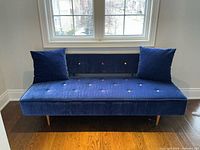 Front view of blue sofa with pillows showing multicolour button tufting and tapered legs