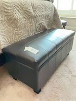 Full view of black faux leather storage bench at foot of bed