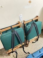 Two folded chairs leaning against wall, showing backs and straps