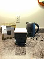 Candle with lid and box next to Krups kettle on countertop