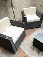 Two black wicker patio armchairs with white cushions on patio