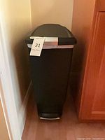 Front view of black plastic simplehuman trash can between cabinets