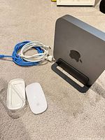 Mac mini standing in vertical stand with Magic Mouse, Ethernet cable, and power/adapter cables visible