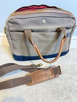 Front view of canvas briefcase showing handles, exterior pocket, navy bottom trim, detachable strap
