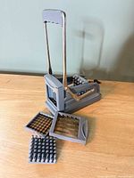 French fry cutter assembled with handle raised; blade inserts and food pusher displayed