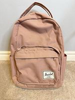 Front view of dusty rose Herschel backpack showing logo patch and front zip pocket