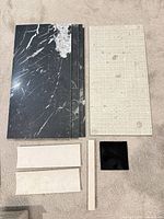 Four glossy black marble-look porcelain tiles, one beige textured tile, limestone bullnose and trim, small black square tile